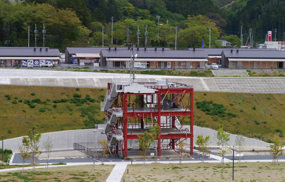 災害遺構として残る「南三陸町防災対策庁舎」と防潮堤と同じ高さで整備された河川堤防。背後に見えるのはかさ上げされた土地に移設された「南三陸さんさん商店街」(南三陸町志津川地区)